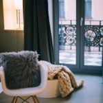 Modern white chair with black pillow and knit blanket by Parisian windows