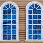 Two symmetrical arched windows with white frames on a tan siding exterior wall